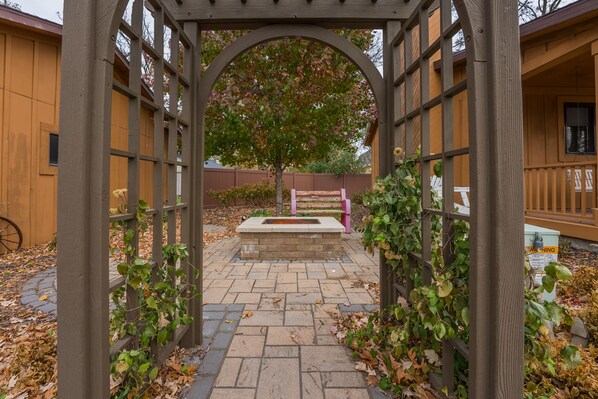 A wooden pergola with a stone bench and a tree in the background. - Retreat in Clear Lake, Iowa - GARAGE HANGOUT - Half block from Lake! (Clear Lake)