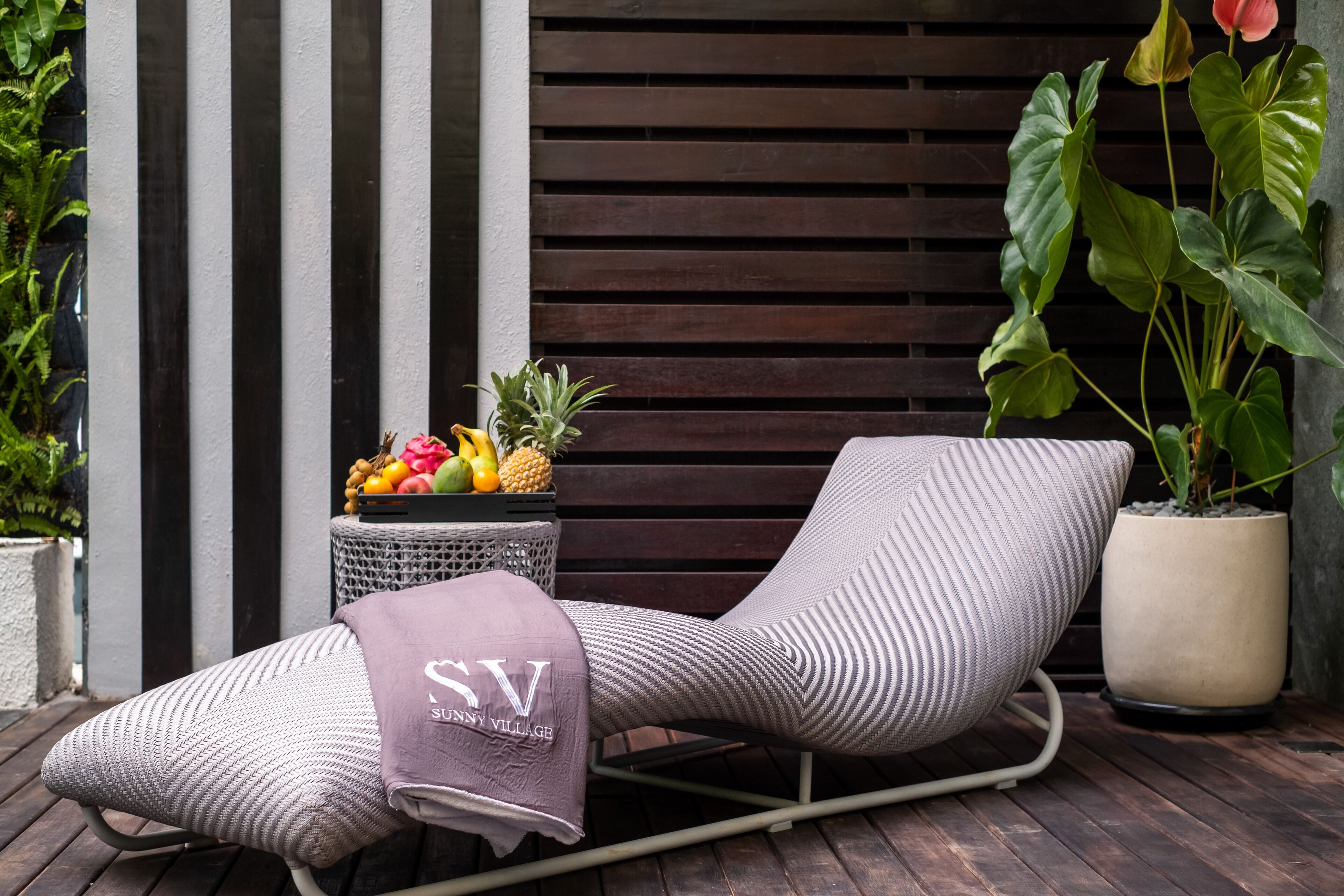 A lounge chair with a cushion, a small side table with fruits, and a potted plant.