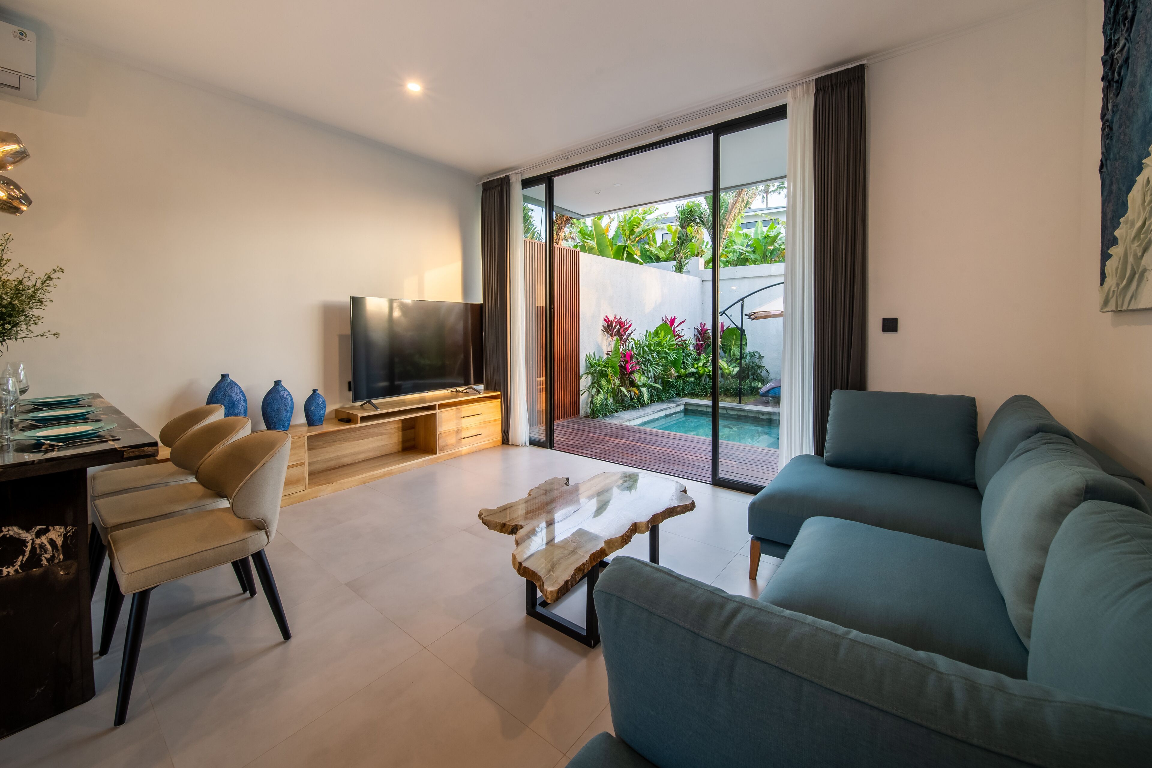 A modern living room with a sofa, a coffee table, a TV, and a dining area with chairs and a table.