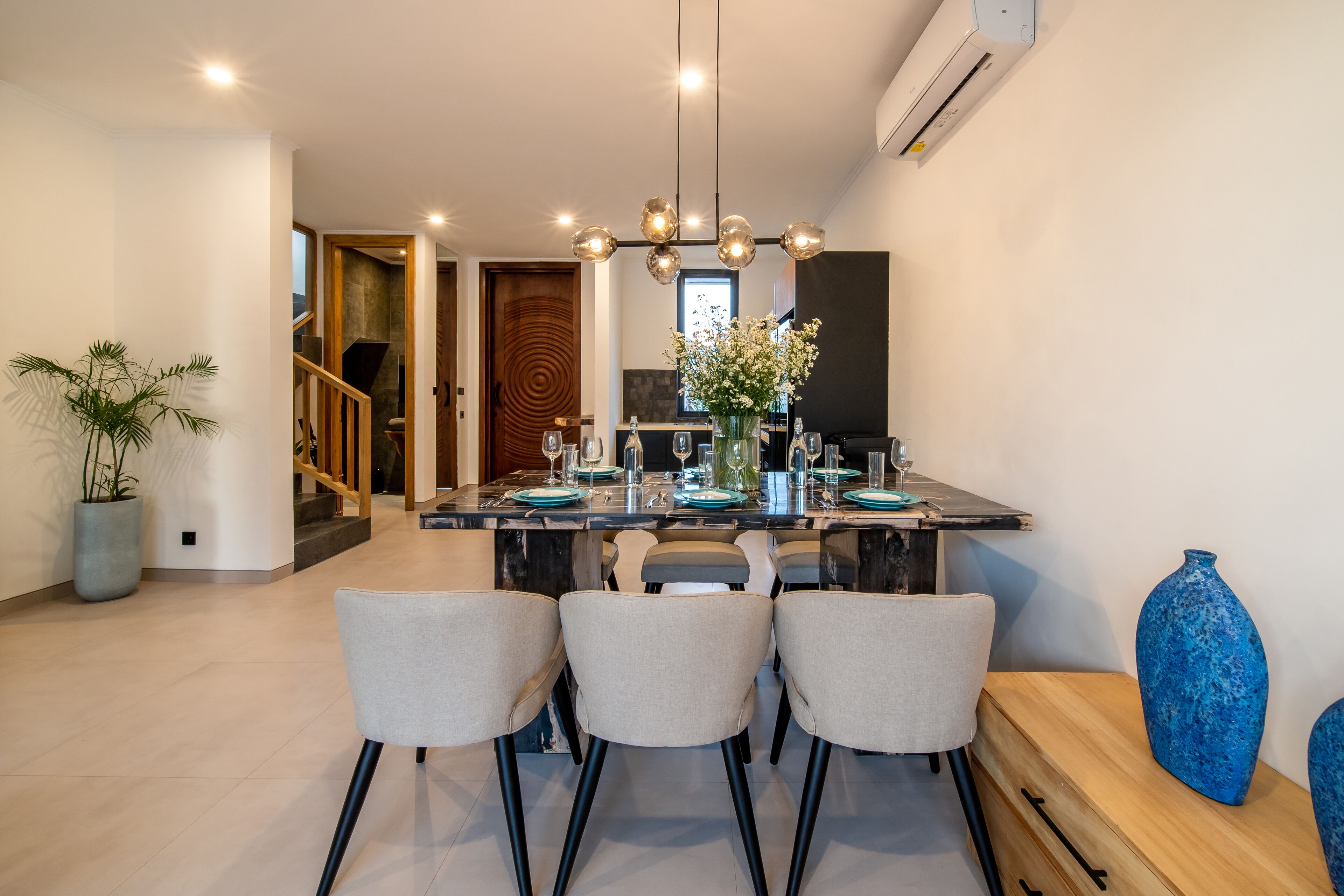A modern dining area with a central island, three chairs, and a vase on the side.