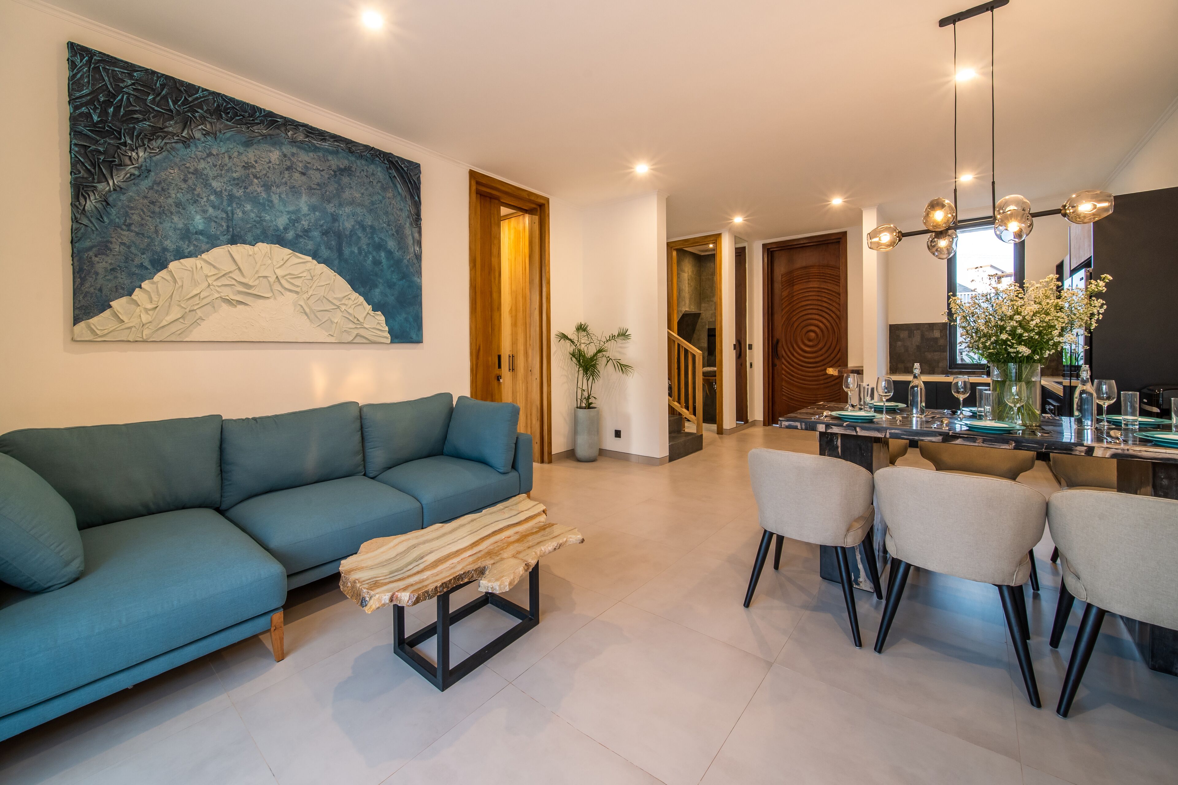 A modern living room with a blue sofa, a wooden coffee table, and a dining area with chairs and a glass-top table.