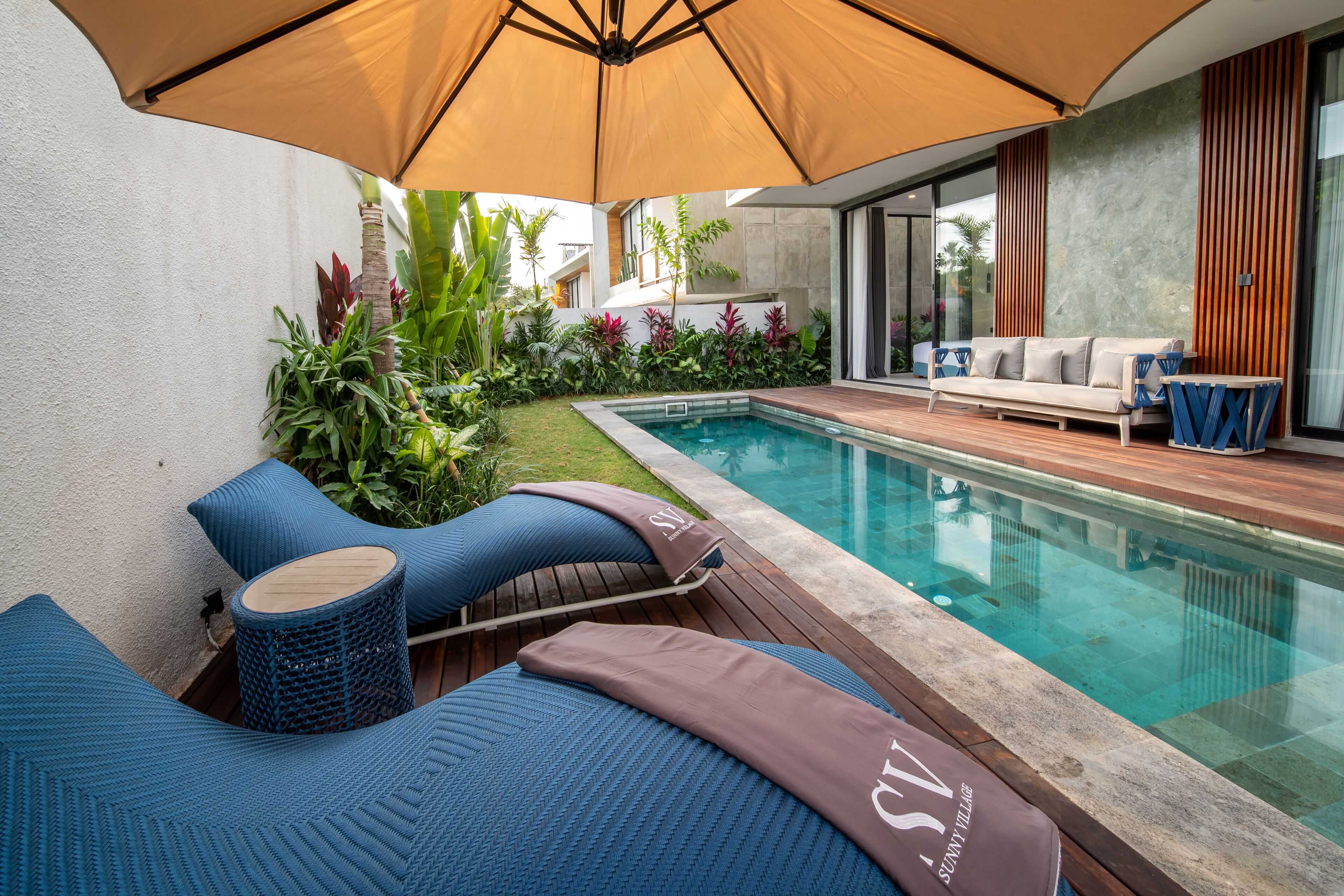 Un área junto a la piscina con sillas de descanso, un sofá y una terraza de madera.