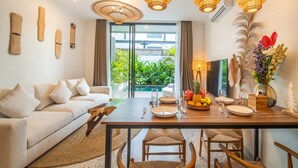 Uma área de refeições moderna com mesa de madeira, sofá branco e cadeiras de vime.
