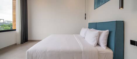 A modern bedroom with a large bed, a view of greenery outside, and a painting on the wall.