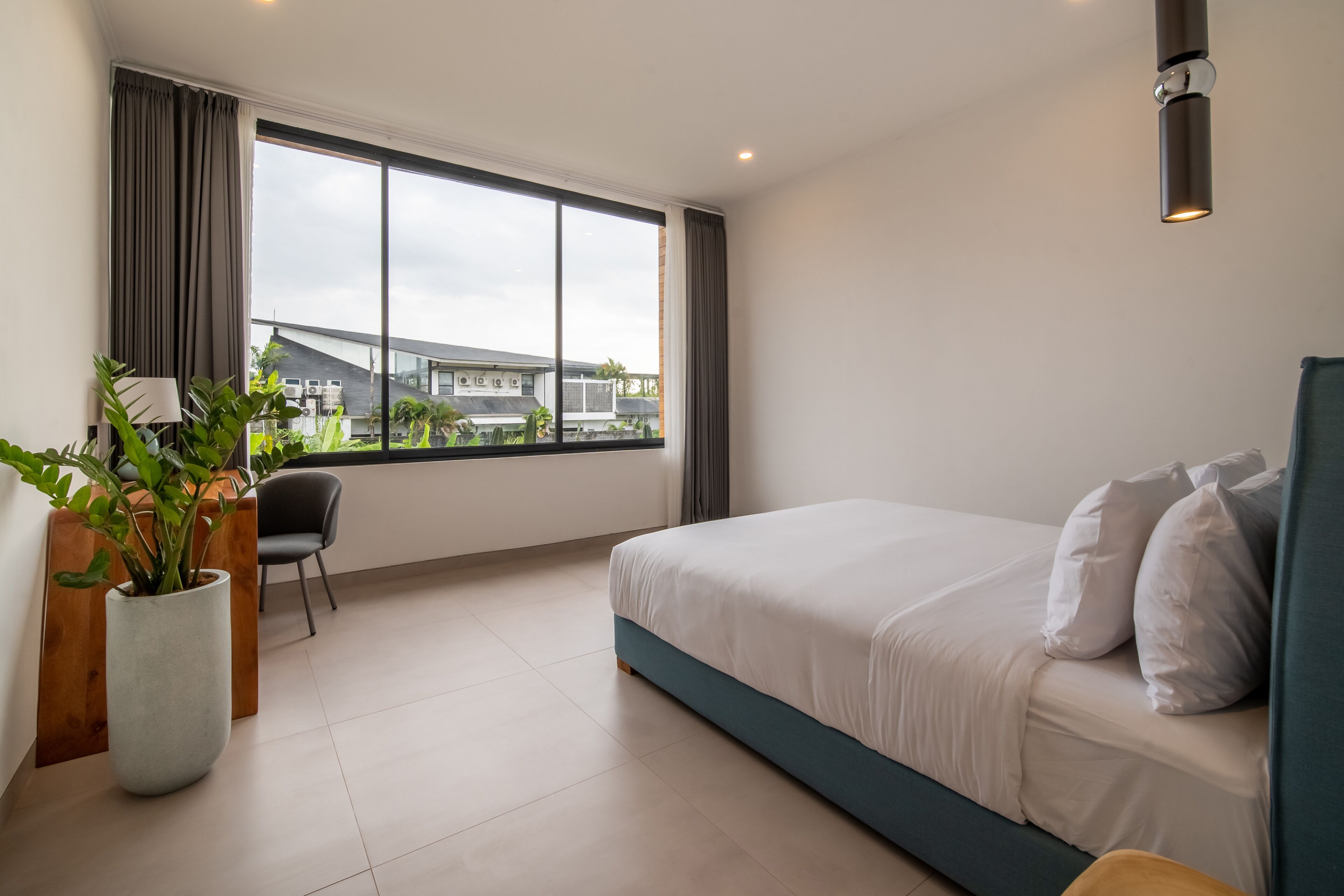 A modern hotel room with a large window, a bed, a desk, and a potted plant.