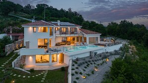 Une maison moderne à deux étages, dotée d’une piscine, de grandes fenêtres et d’un mur de soutènement en pierre.