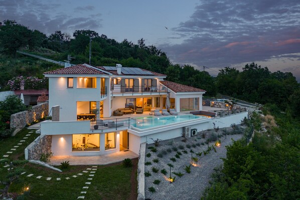 Una casa moderna de dos pisos con piscina, ventanas amplias y un muro de contención de piedra.
