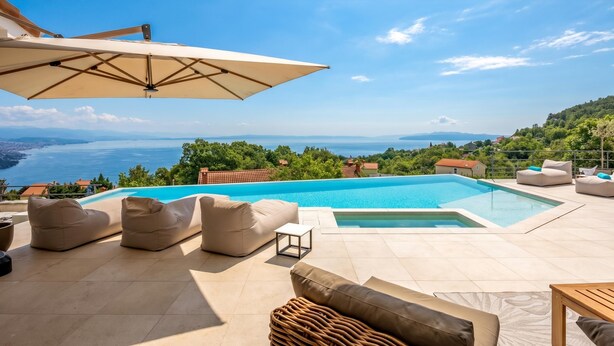 Un espace aménagé au bord de la piscine, avec des sièges et une vue sur la mer.