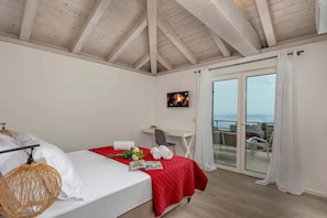 Une chambre à coucher comprenant un lit, un bureau, une chaise, un téléviseur et un balcon avec des rideaux.