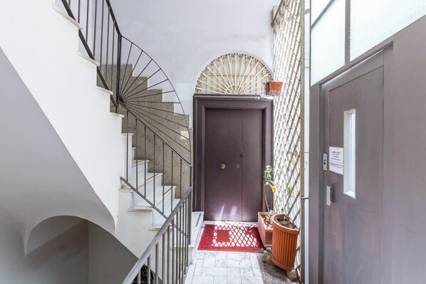 A narrow hallway with a spiral staircase on the left, a dark door at the end, and a red mat at the entrance. - Chiaia Relax on Pedastrian Area (Naples)