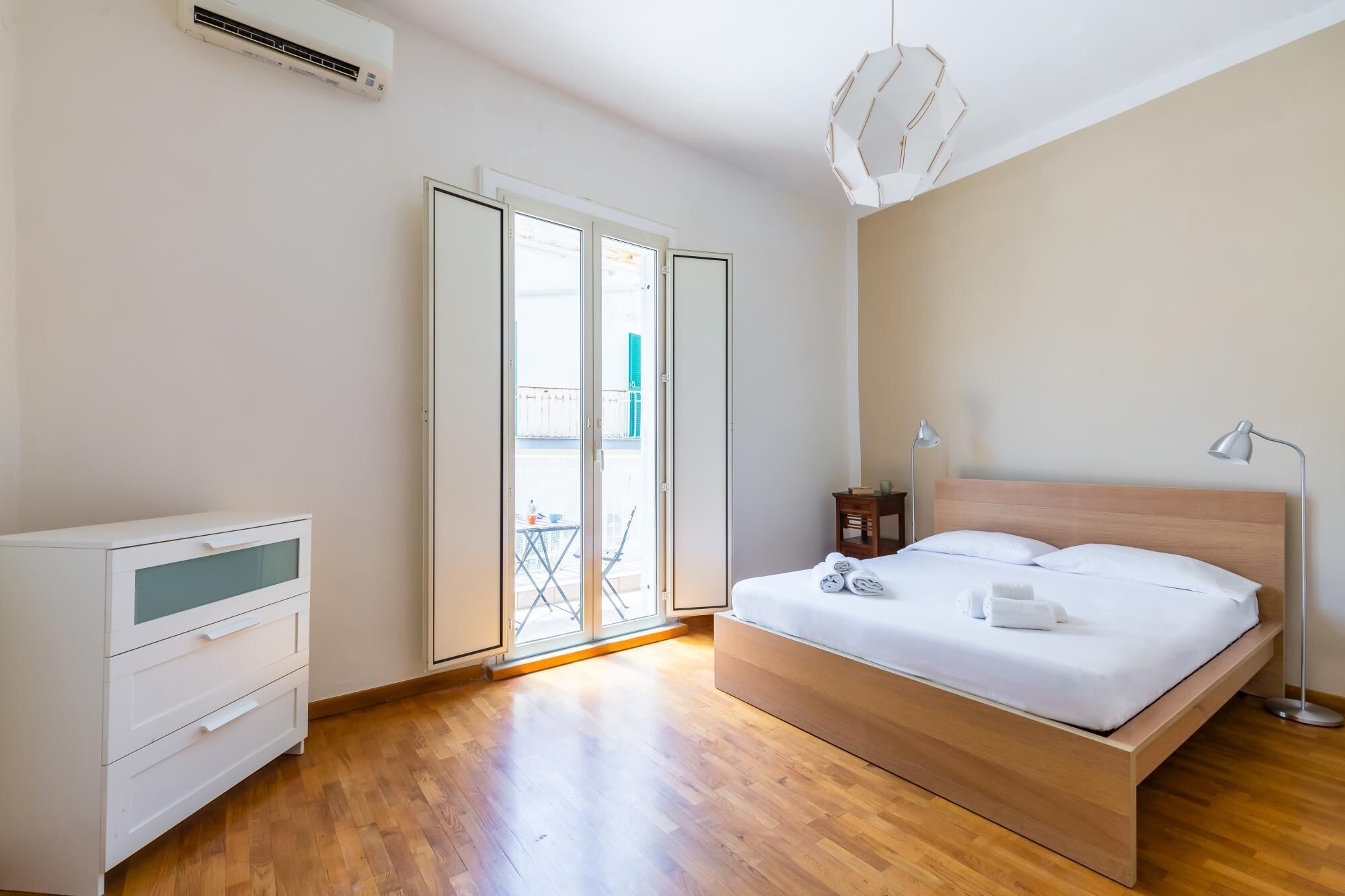 A bedroom with a wooden bed, a desk, and a chair. There is a sliding glass door leading to an outdoor area.