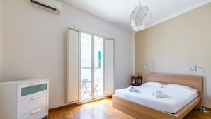 Ein Schlafzimmer mit einem hölzernen Bett, einem Schreibtisch und einem Stuhl. Eine Glastür führt zu einem Außenbereich.