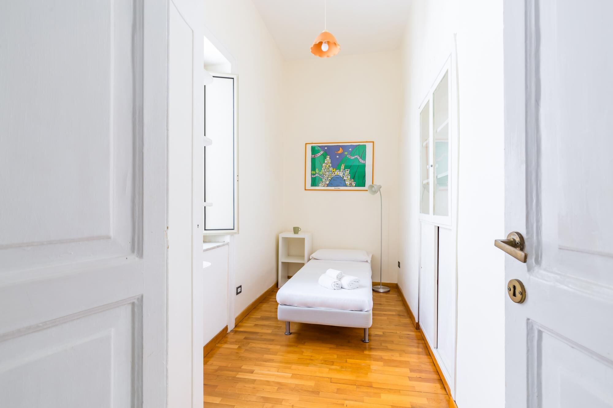 A narrow hallway with a bed, a bedside table, and a wall-mounted picture.