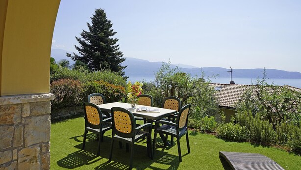 Um pátio com mesa e cadeiras, com vista para um corpo de água e montanhas.