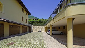 Rua de paralelepípedos estreita, ladeada por edifícios amarelos, com carros estacionados e uma scooter.