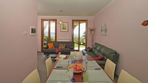 Uma sala de jantar com mesa posta para quatro pessoas, um sofá e vista para o exterior.