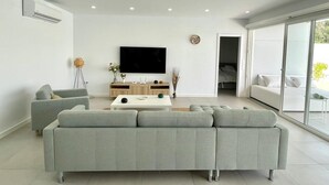 Een moderne woonkamer met een grijze bank, een flatscreentelevisie en een groot raam.