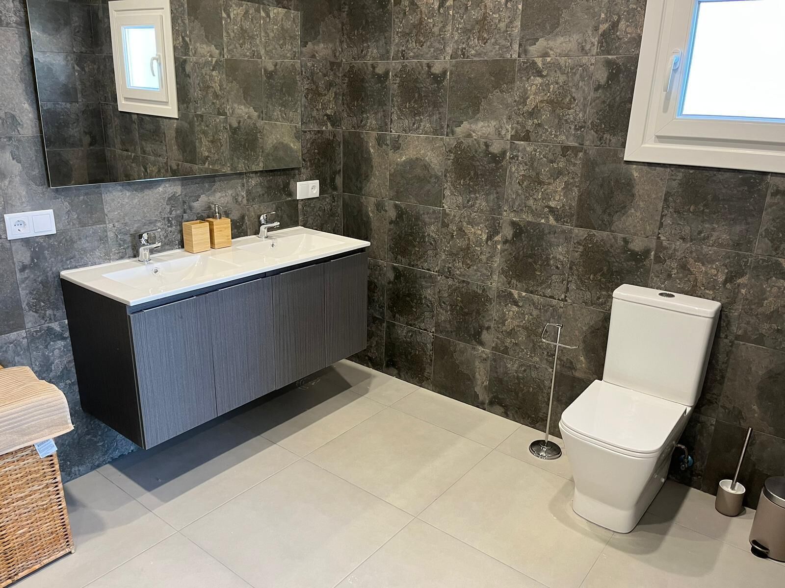 Un baño moderno con una pared de piedra oscura, un lavabo blanco y un inodoro.