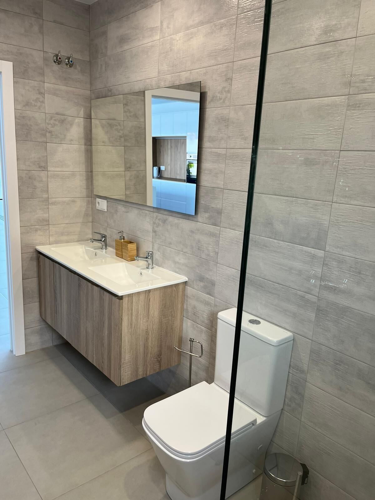 A modern bathroom with a wooden vanity, a large mirror, a toilet, and a glass shower enclosure.