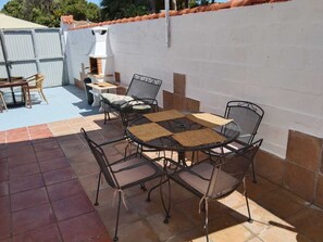 Eine Terrasse im Freien mit einem runden Tisch, vier Stühlen, einem kleinen weißen Tisch und einem Grill.