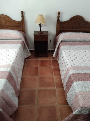 Ein Zimmer mit zwei Betten, einem Nachttisch mit Lampe und einem gefliesten Boden.