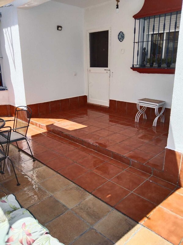 Un patio con suelo de baldosas, una puerta, una mesita y una silla.