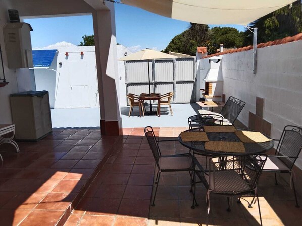 An outdoor patio with a table and chairs, a grill, and a view of the sea.