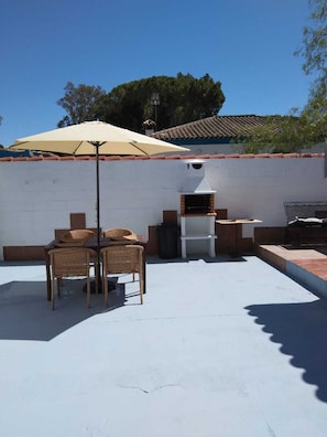Eine Terrassenanlage im Freien mit Grill, Korbstühlen und einem Tisch unter einem großen Sonnenschirm.