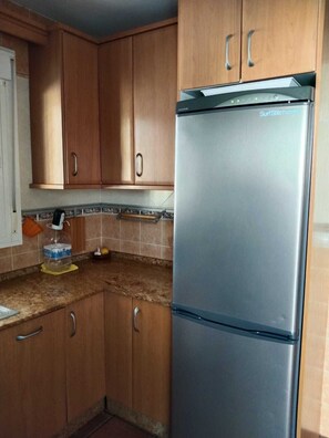 Eine Küche mit Holzausstattung, einem Edelstahlkühlschrank und einer gefliesten Spritzschutzwand.