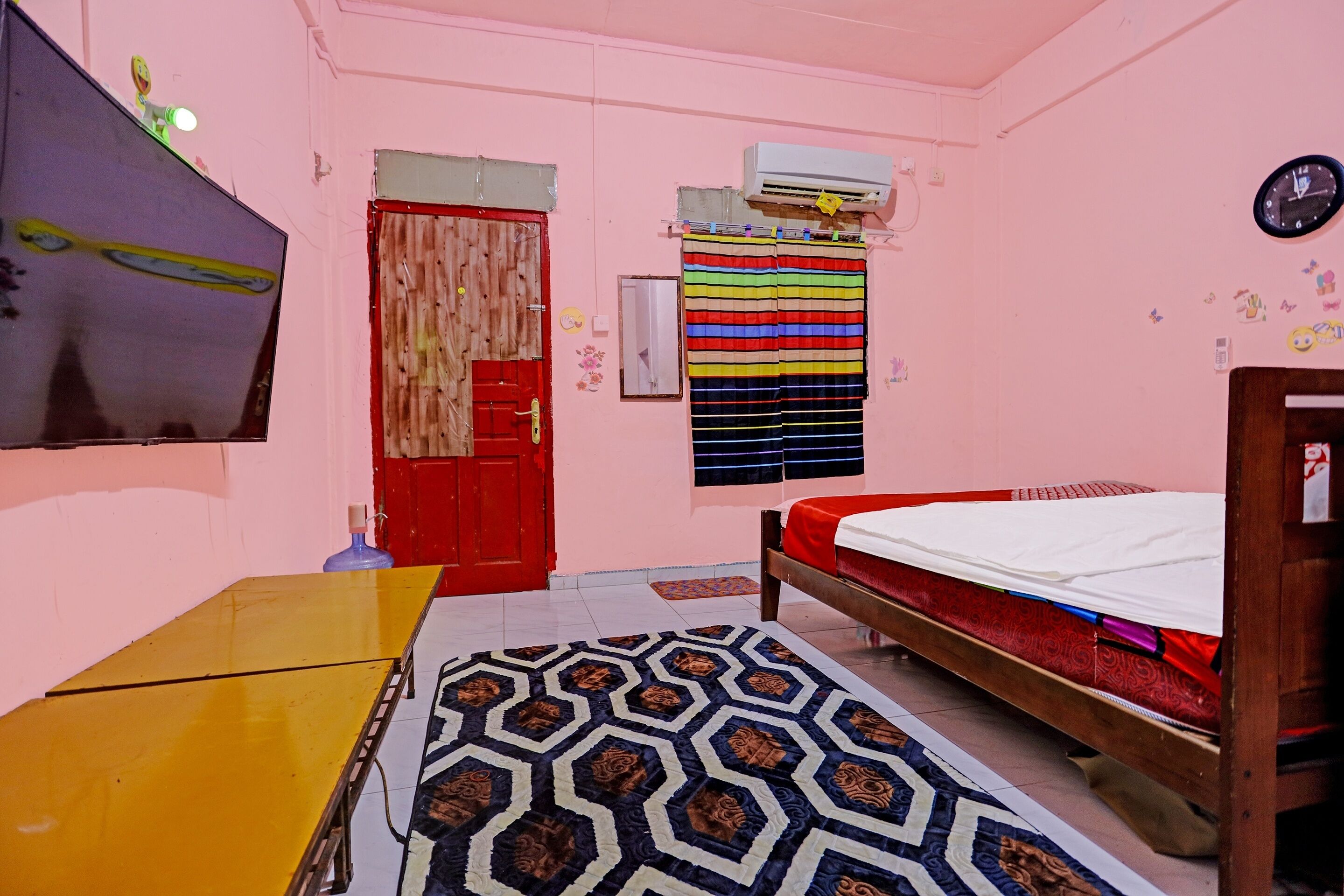 A room with a bed, a desk, a window with curtains, an air conditioning unit, and a wall clock.