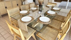 A dining area with a glass-top table, woven chairs, and a kitchen in the background.