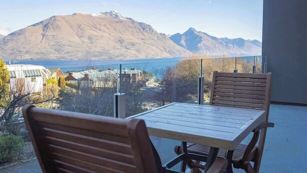 A balcony with a table and chairs, overlooking a mountainous landscape and a body of water.