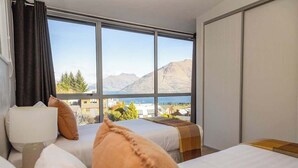 A hotel room with two beds, a window with a mountain view, and a lamp on the left side.