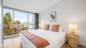 A bedroom with a large bed, two bedside tables, a window with a view, and a wall-mounted artwork.