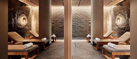 A spa room with wooden loungers, a central pillar, and a textured wall with a light fixture.
