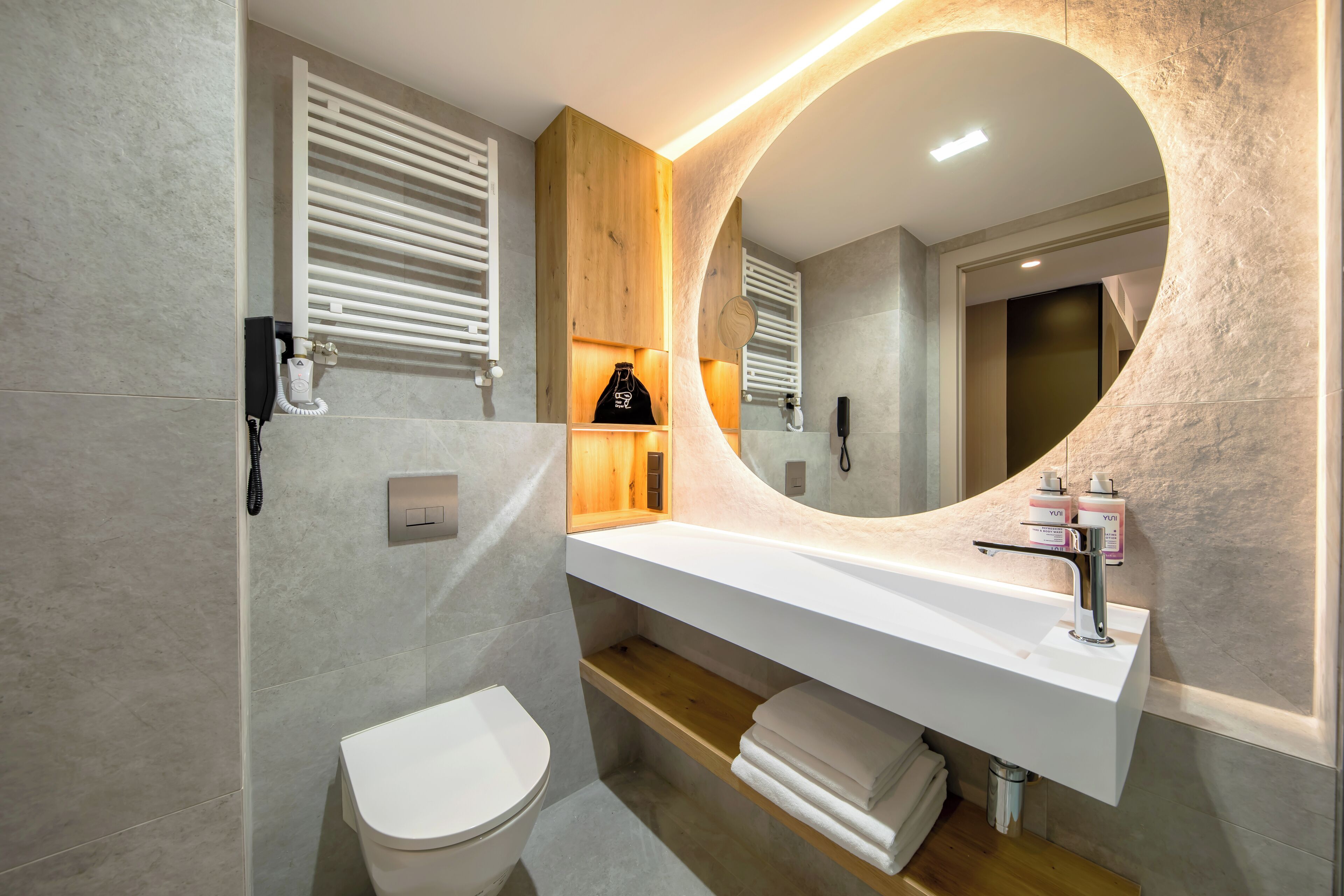Ein modernes Badezimmer mit einem weißen Waschbecken, einem Holzschranken und einem großen Spiegel.