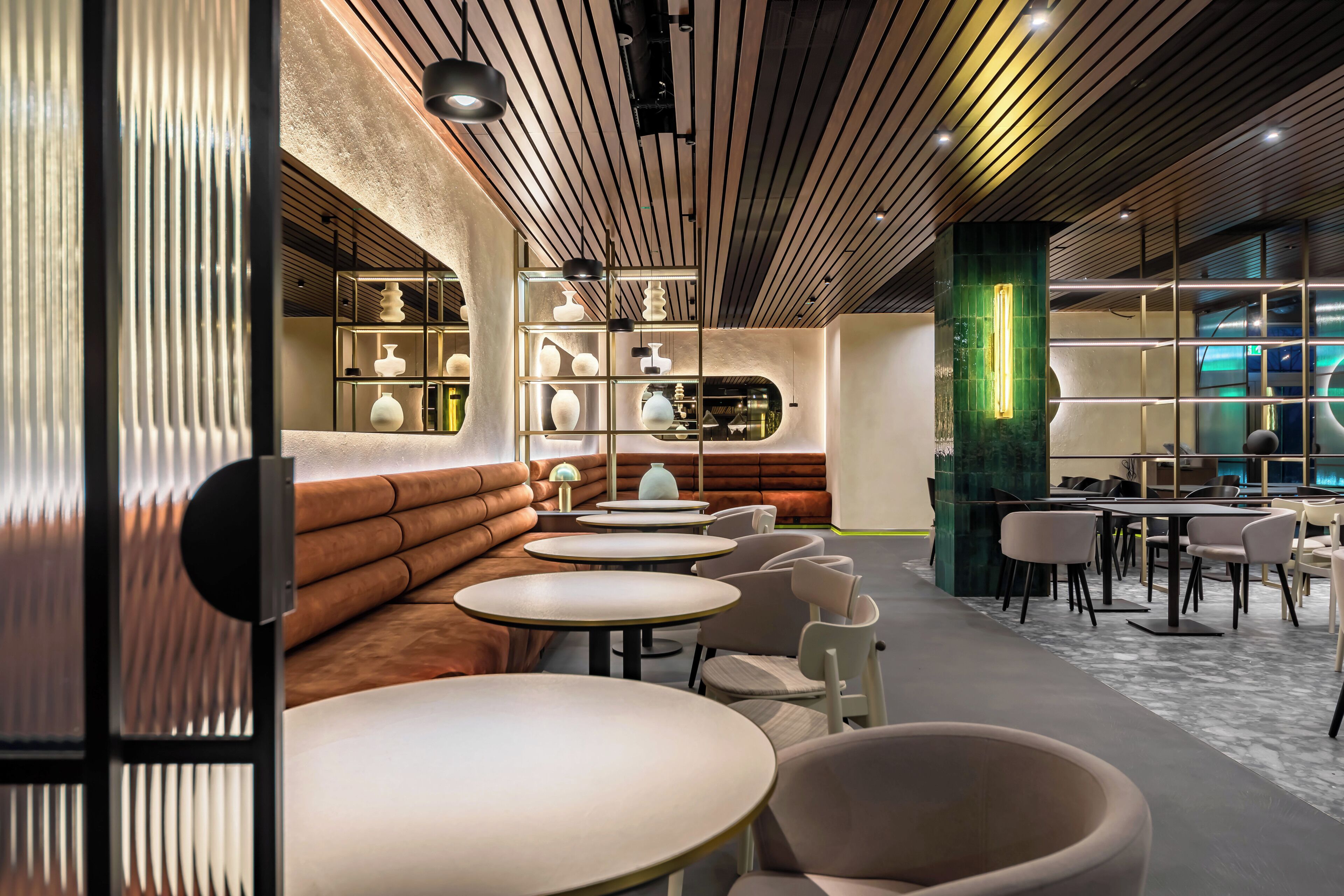 A modern interior with round tables and cushioned seating, a green accent wall, and a display of decorative items.