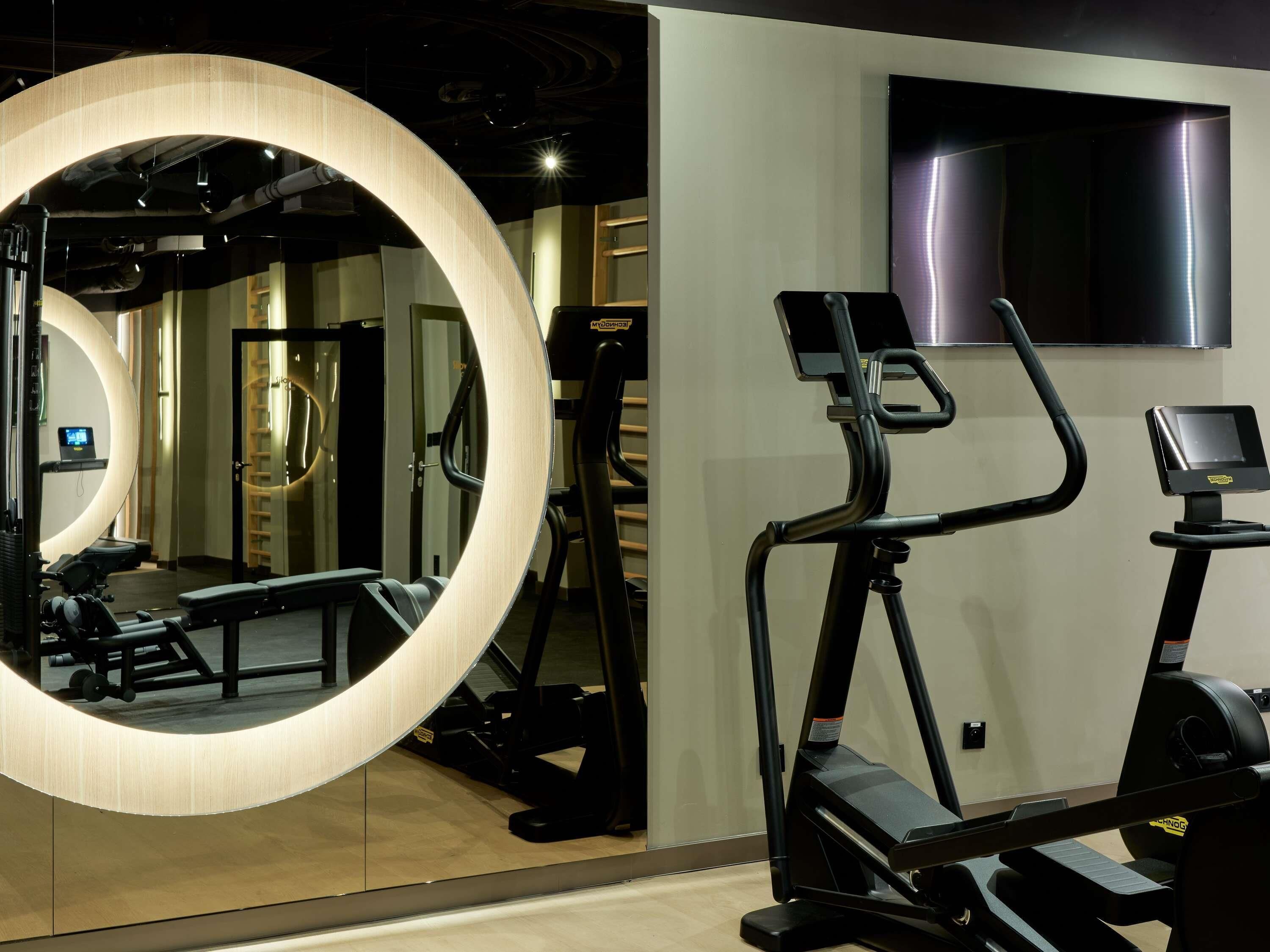 Ein Fitnessraum mit Trainingsgeräten, einem großen Spiegel und einem Fernseher an der Wand.