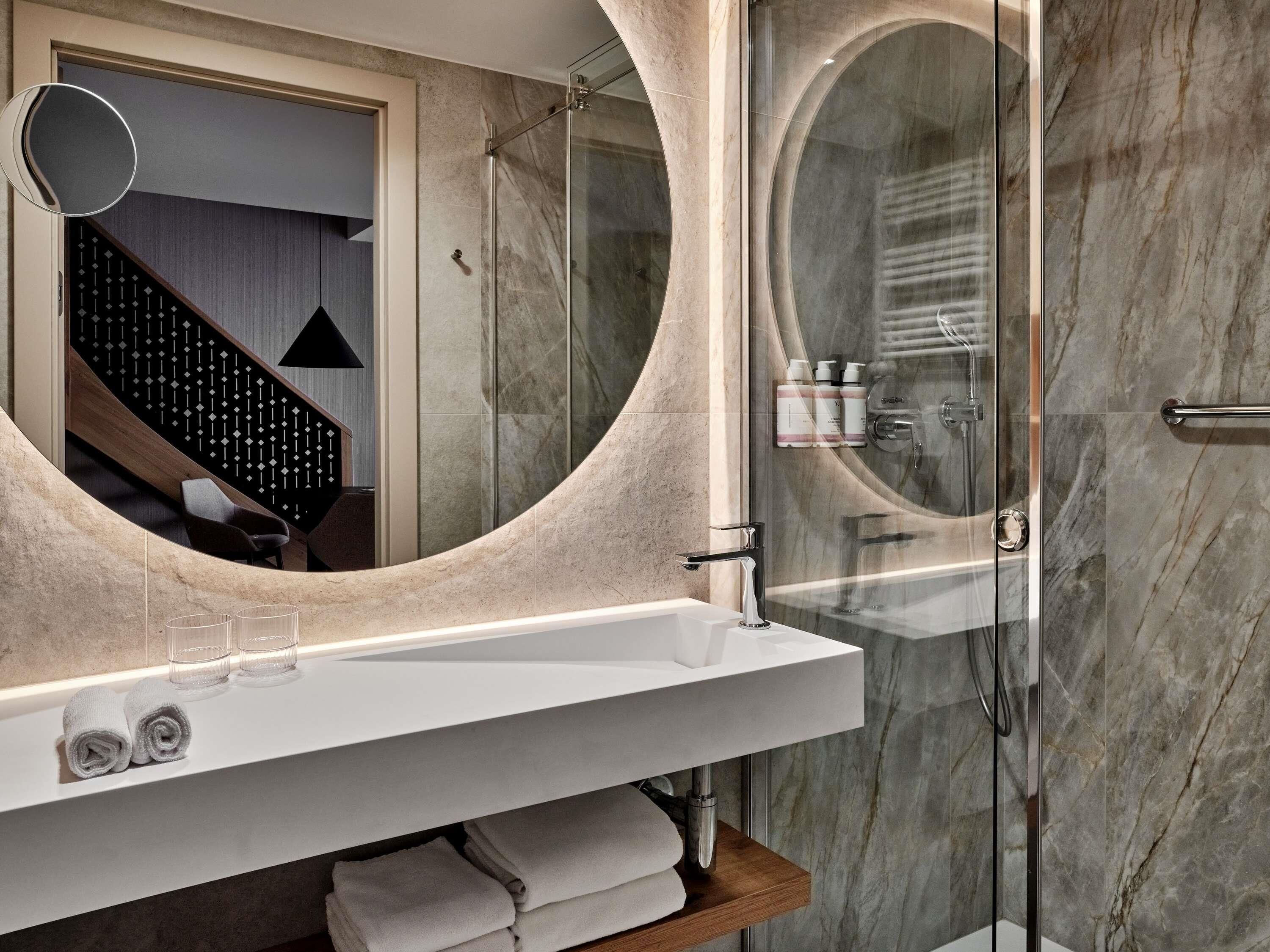 Une salle de bain moderne avec un grand miroir, une douche à parois de verre, un lavabo blanc et des serviettes soigneusement pliées.