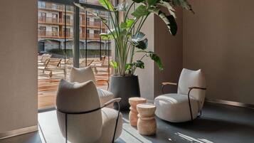 Un interior modern amb dues cadires còmodes, una planta gran en test i vistes a zones d'estar exteriors a través de grans finestres.