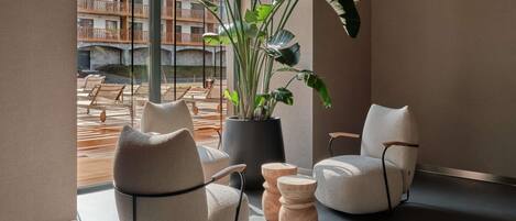 Un interior moderno con dos sillones cómodos, una planta grande en maceta y vistas a una zona de estar exterior a través de amplios ventanales.