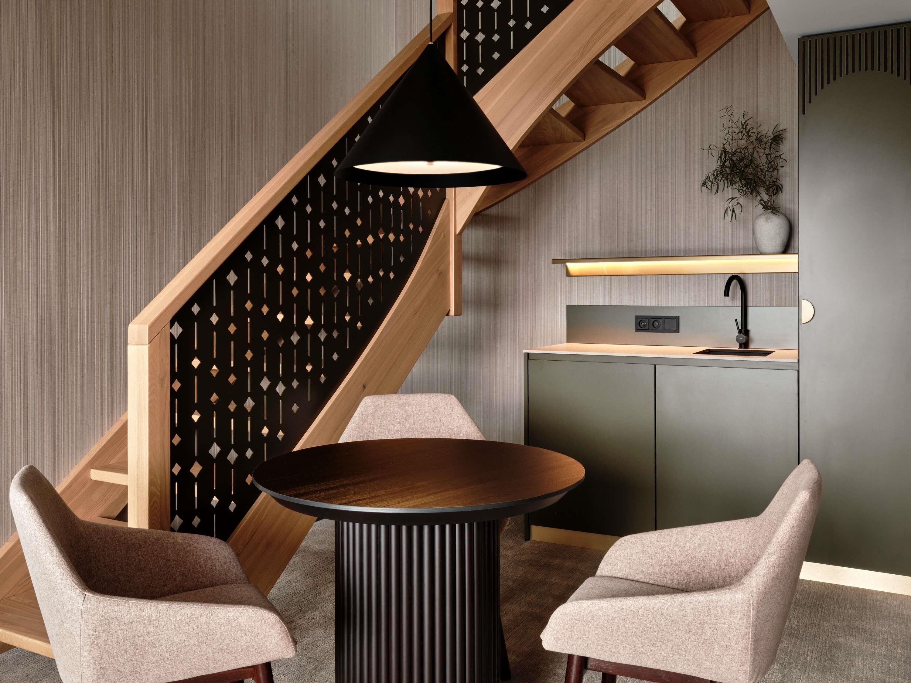 A modern kitchen with a built-in stove, a sink, and a wooden staircase with a geometric patterned wall.