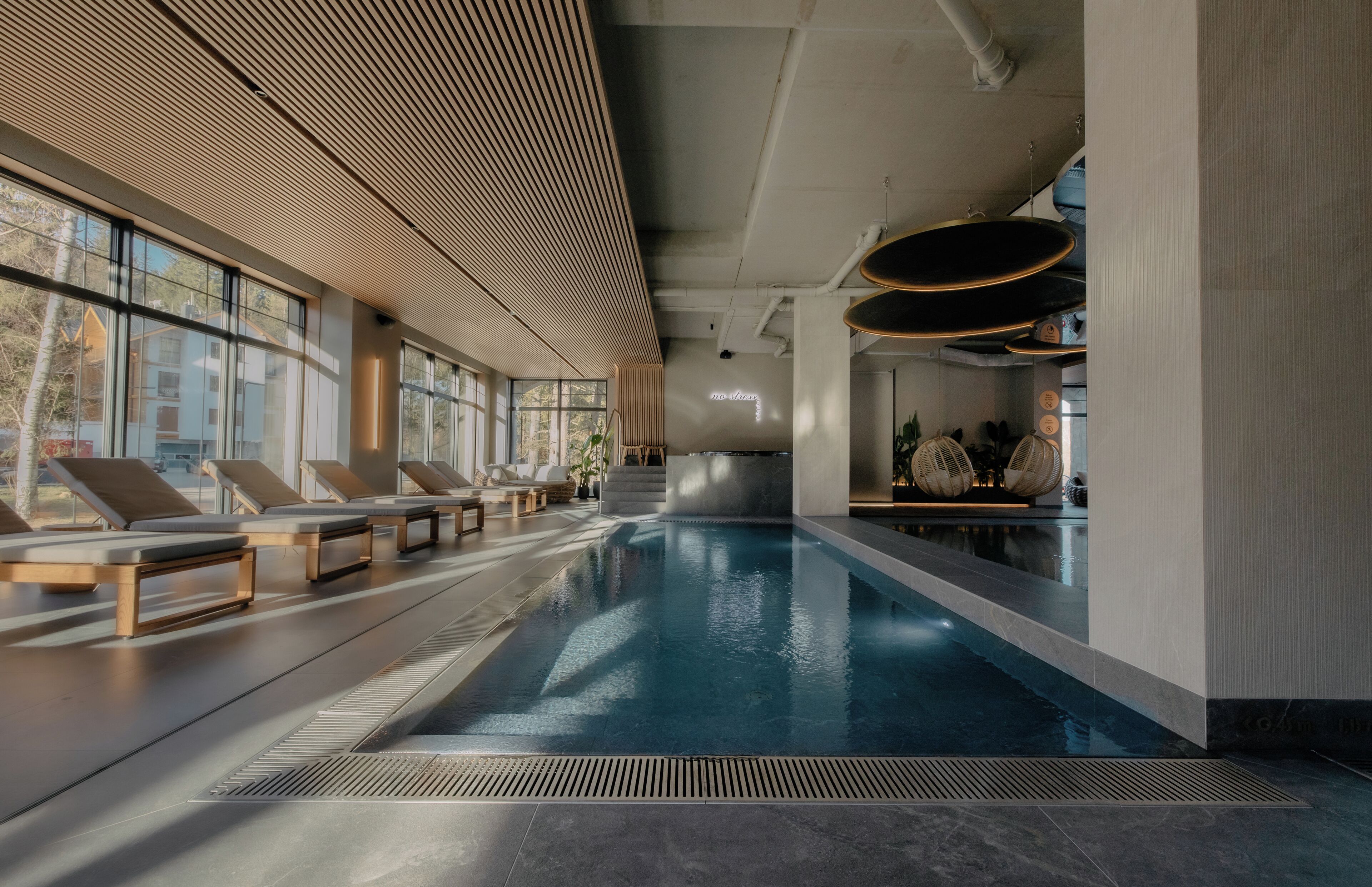 Uma piscina interior moderna com espreguiçadeiras e vista para o exterior.