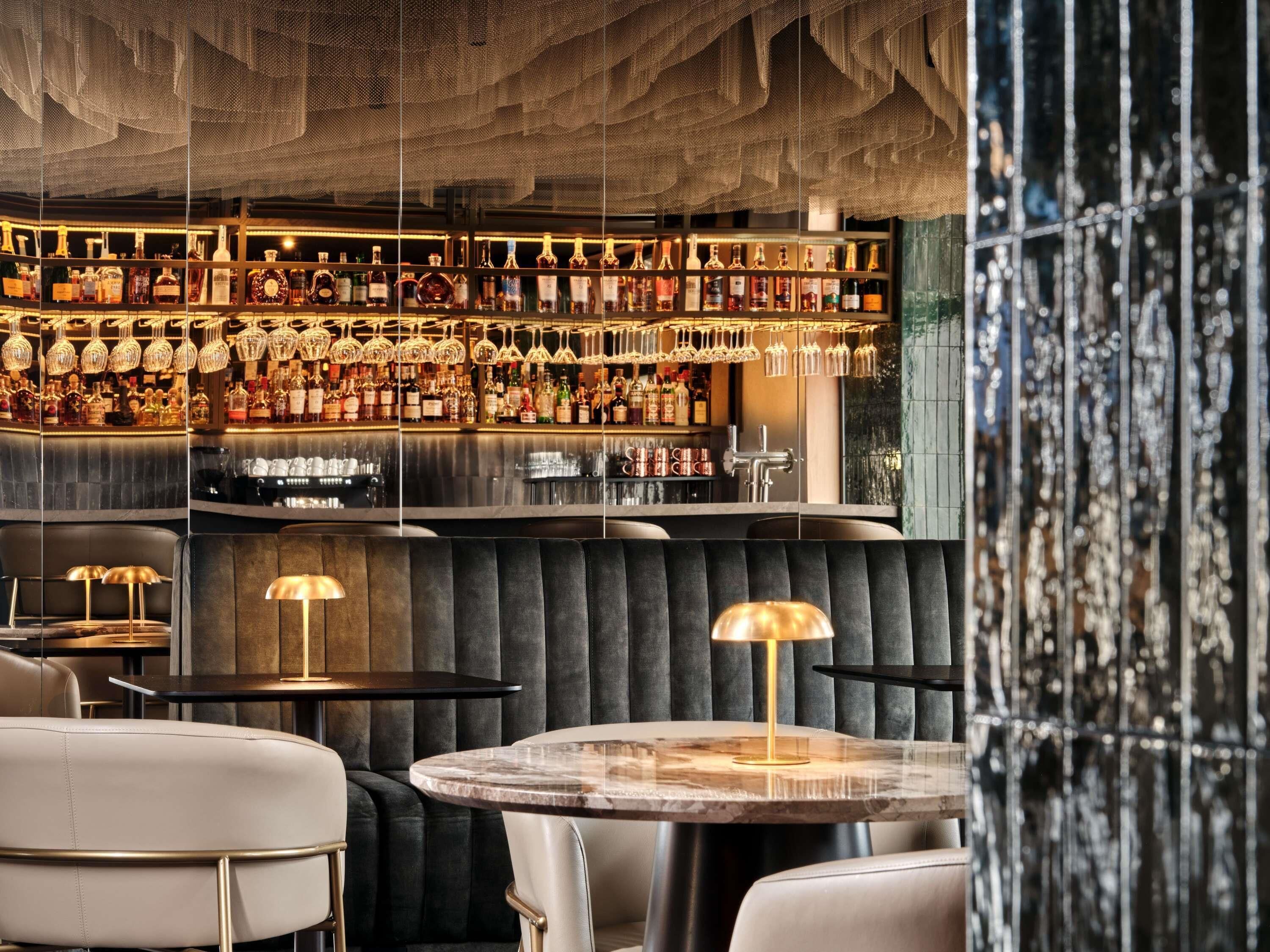 A bar area with a variety of liquor bottles, hanging glasses, and seating with tables and chairs.