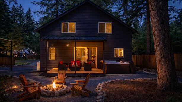 A dark wooden cabin with a covered porch, outdoor seating, and a fire pit.