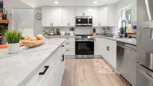 A modern kitchen with white cabinets, stainless steel appliances, and a wooden floor.