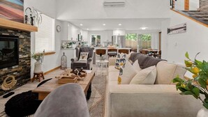 A spacious living room with a fireplace, a dining area, and a kitchen in the background.