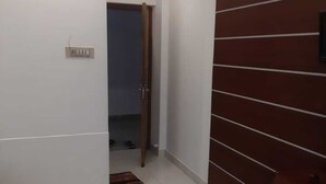 A hallway with a white wall, a wooden door, and a tiled floor. - Hotel Shalimar Residency (Kanayannur)