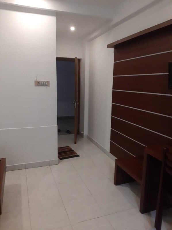 Un pasillo con pared blanca, puerta de madera y suelo de baldosas.