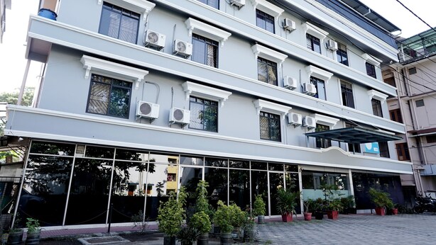 A multi-story building with large windows, air conditioning units, and potted plants in the entrance area. - Hotel Shalimar Residency (Kanayannur)